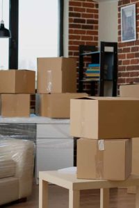 Nobody in empty living room with cardboard packaging at new home, furniture things in stack of carton boxes. No people in household property with package cargo to move in, real estate.